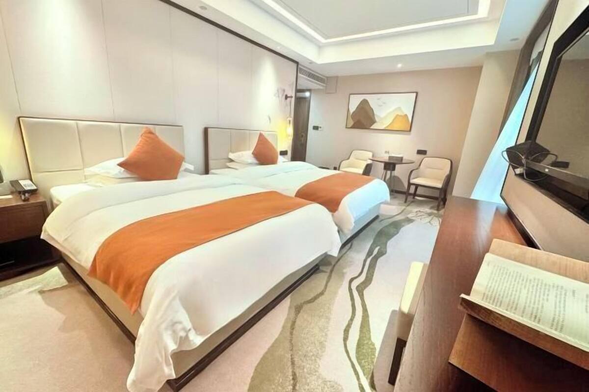 A hotel room with two beds, a desk, a chair, and a painting on the wall.