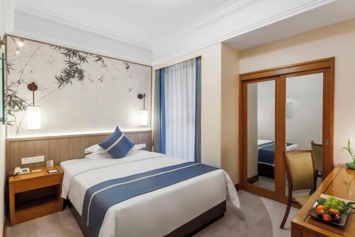 A hotel room with a bed, bedside table, lamp, and a view through a door.