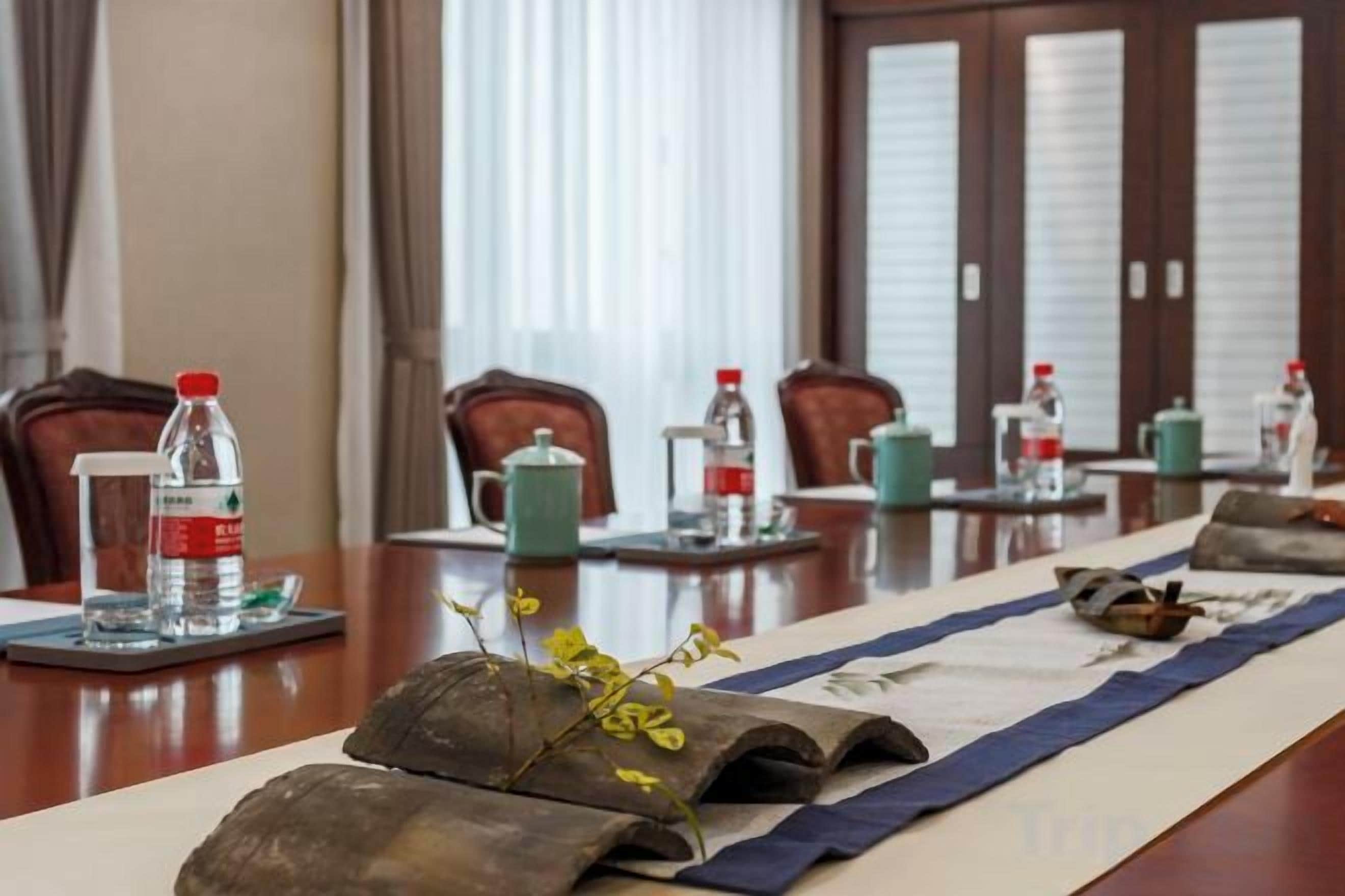 A conference room with a long table, chairs, water bottles, and a decorative vase.