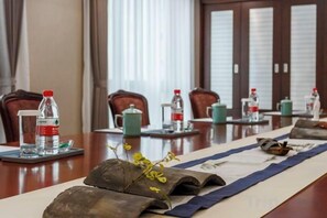 Un salón de conferencias con una mesa larga, sillas, botellas de agua y un jarrón decorativo.