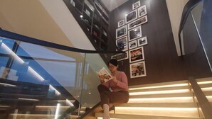 A person sitting on a staircase with a magazine, surrounded by framed pictures on the wall. - Hangzhou Wenhua GINLAN JIA Grand Hotel (Hangzhou)