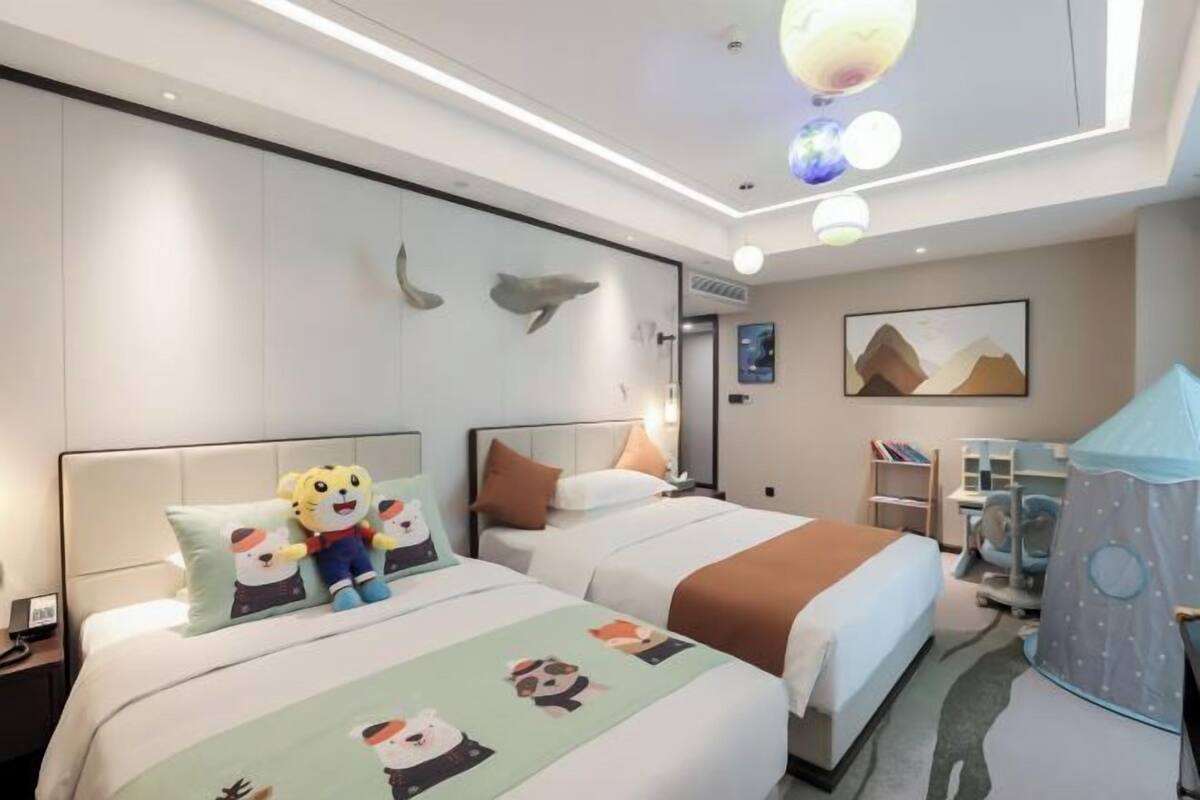 A hotel room with two beds, a desk, a chair, a bookshelf, a tent-like structure, and wall art.