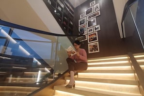 A person sitting on a staircase with a book, surrounded by framed pictures on the wall.
