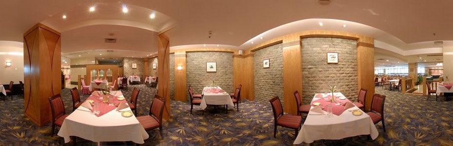 Uma sala de jantar de hotel com mesas redondas, cadeiras e piso coberto por carpete.