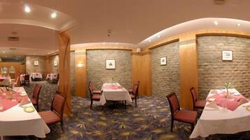 Uma sala de jantar de hotel com mesas redondas, cadeiras e piso coberto por carpete.