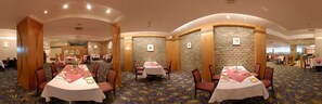 Un comedor de hotel con mesas redondas, sillas y suelo alfombrado.