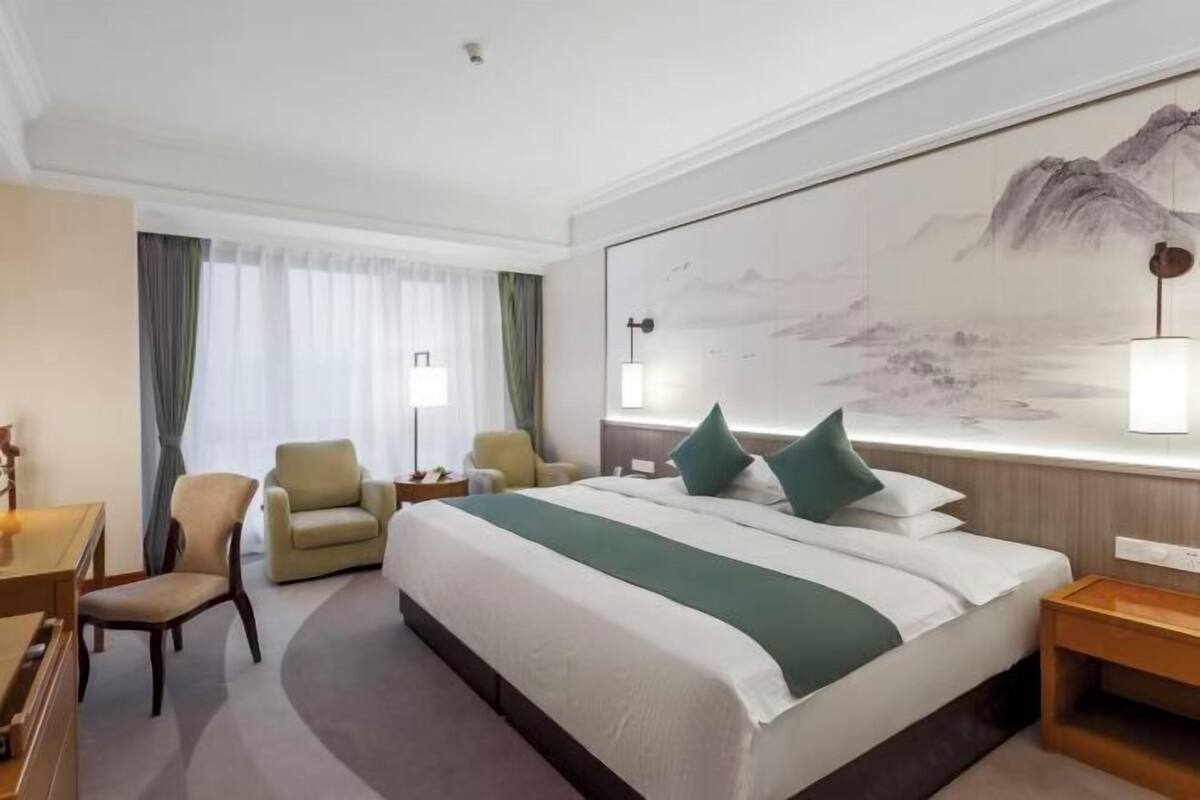 A hotel room with a large bed, two chairs, a desk, and a painting on the wall.