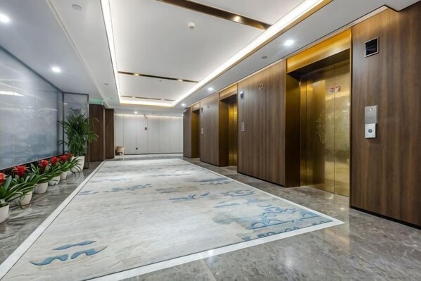 Un vestíbulo de hotel con suelo de mármol, paneles de madera y dos ascensores.