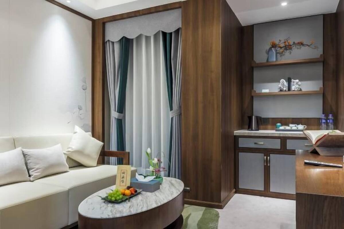 A modern living room with a sofa, a round coffee table with fruits, a small side table, and a kitchen area with a counter and cabinets.