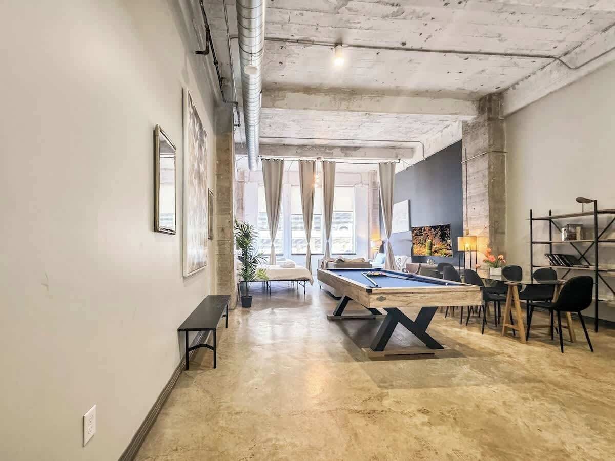 A spacious room with a pool table, a sofa, and a dining area with chairs.