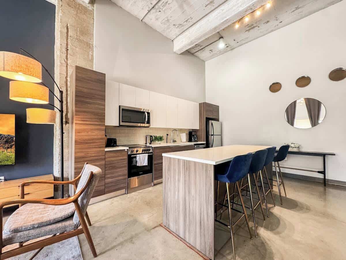 A modern kitchen with a central island, bar stools, and a dining table with chairs.
