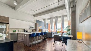 Une cuisine moderne avec des tabourets de bar, un coin repas avec une table et des chaises, et une grande fenêtre avec des rideaux.