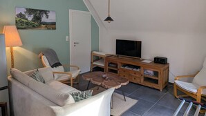 Ett vardagsrum med en soffa, fåtöljer, en tv, en träskommod och en lampa.