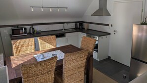 Ett kompakt kök med ett matbord, stolar, en mikrovågsugn, en kaffebryggare och ett kylskåp i rostfritt stål.