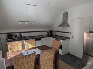 Eine kompakte Küche mit Esstisch, Stühlen, einer Mikrowelle, einer Kaffeemaschine und einem Edelstahlkühlschrank.
