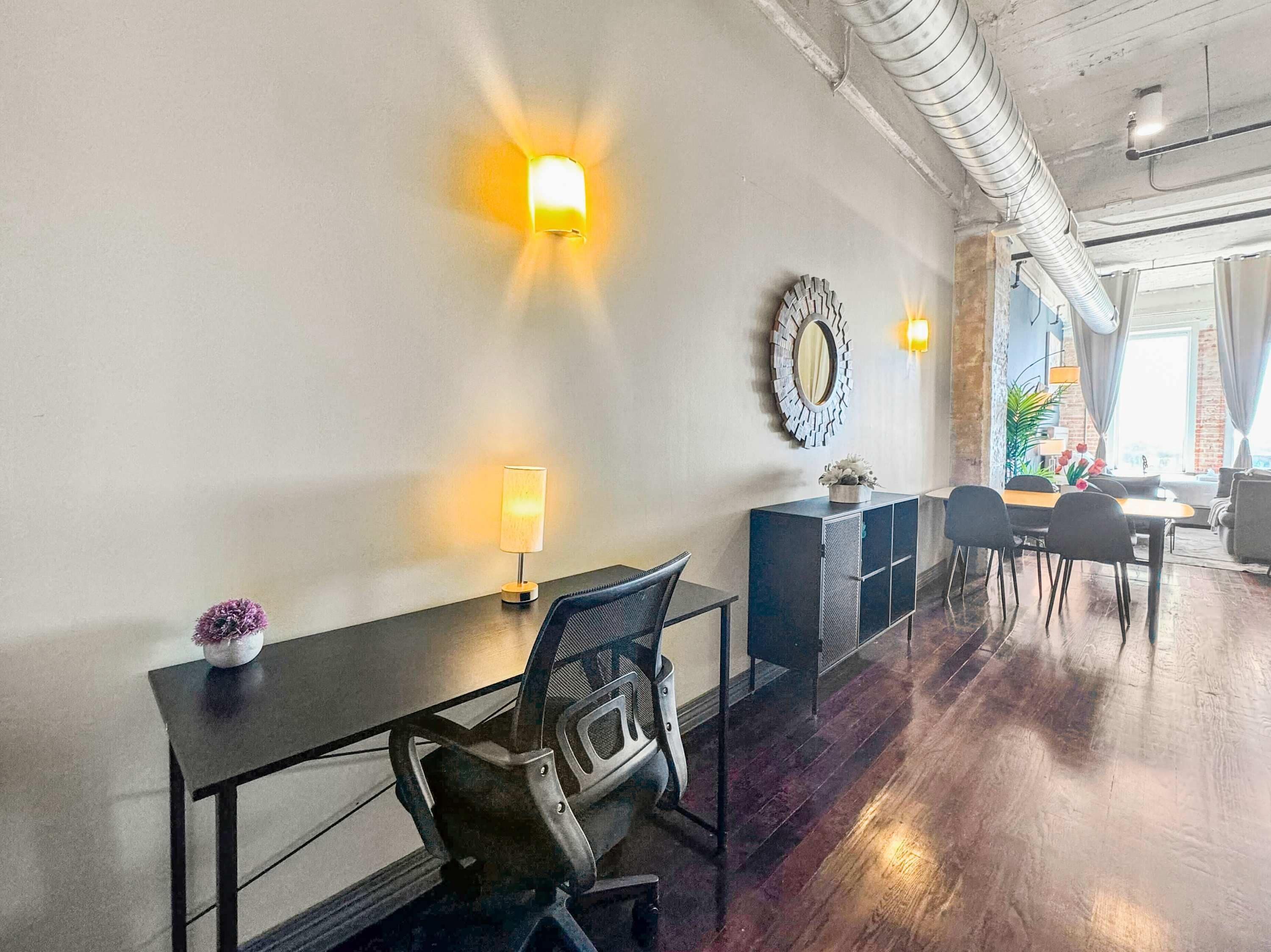 Un espace repas moderne avec une table noire, des chaises et un miroir décoratif au mur.