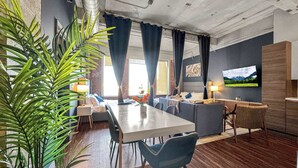 Una sala de estar moderna con comedor, televisor montado en la pared y un gran ventanal con cortinas.