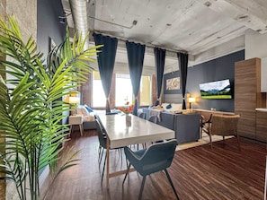 Una sala de estar moderna con comedor, televisor montado en la pared y un gran ventanal con cortinas.
