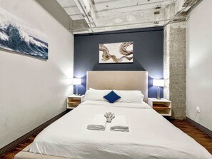A hotel room with a bed, two bedside lamps, a painting on the wall, and a towel on the bed.