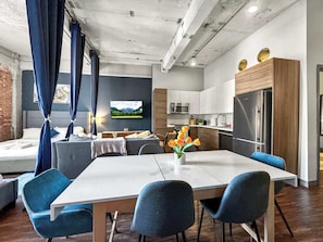 Una sala de estar moderna con un sofá, una mesa de comedor y sillas. Cuenta con una zona de cocina con refrigerador y microondas.