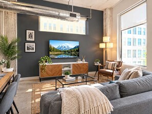 En moderne stue med et stort fladskærms-tv, en sofa, et sofabord og et spiseområde med en plante.