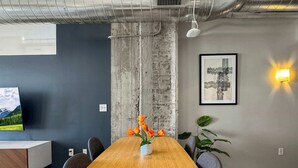 A conference room with a wooden table, chairs, a vase with flowers, a framed picture, and a wall-mounted light.