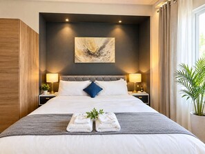 A hotel room with a large bed, two bedside lamps, a wall-mounted painting, and a potted plant.