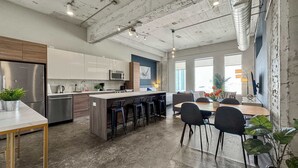 A modern kitchen with stainless steel appliances, a central island with bar stools, and a dining area with a large table and chairs.