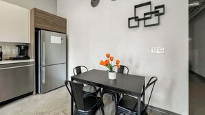 A modern kitchen with a stainless steel refrigerator, a dining table with four chairs, and a vase with orange flowers.