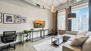 A modern living room with a large window, a sofa, a coffee table, and a TV on the wall.