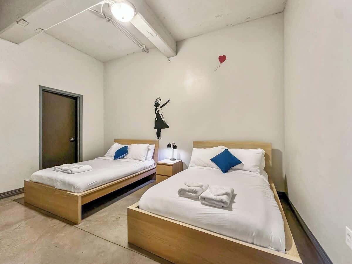 Een hotelkamer met twee eenpersoonsbedden, een houten hoofdbord, wit beddengoed, een nachtkastje met een lamp en een wandlamp.