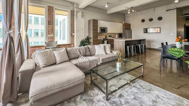 A spacious living area with a large sofa, a glass coffee table, and a dining area with chairs and a table.