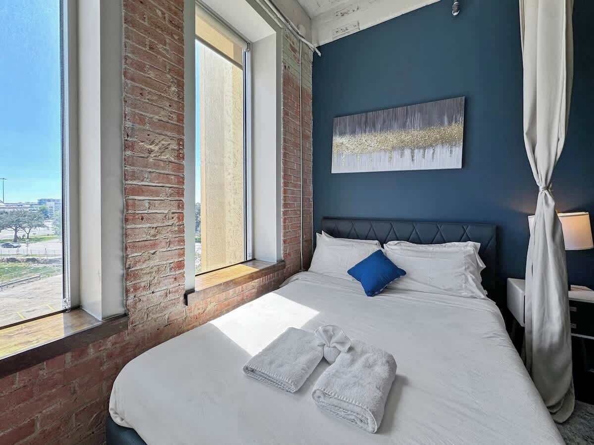 Una habitación de hotel con una cama grande, vistas al exterior y una pared de ladrillo.