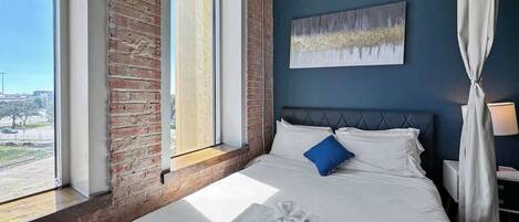 Una habitación de hotel con una cama grande, vistas al exterior y una pared de ladrillo.