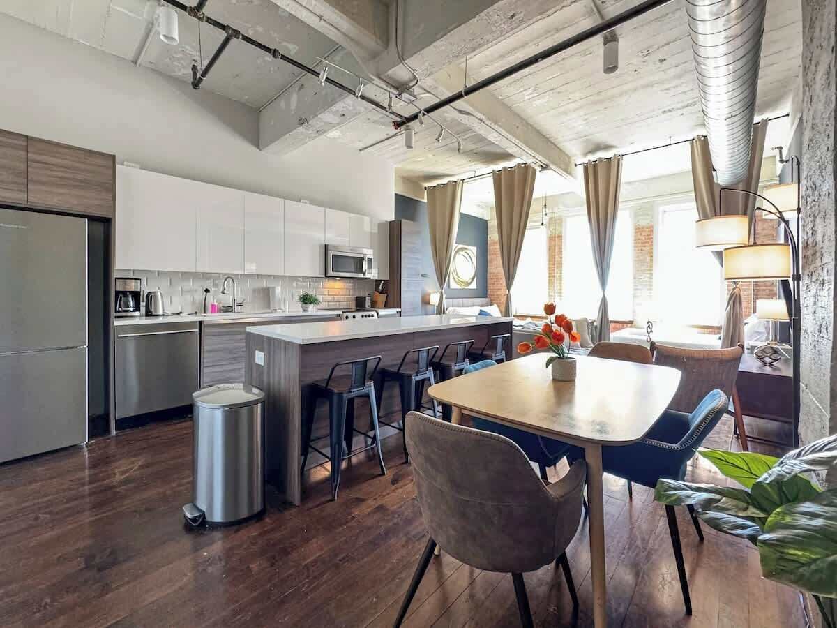 A modern kitchen with a central island, bar stools, and a dining table with chairs.