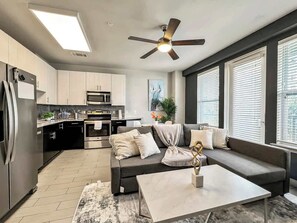 A modern kitchen with a built-in oven and microwave, a dark-colored sofa with cushions, a coffee table, and a ceiling fan.