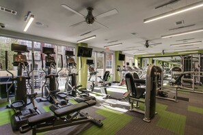 Une salle de sport équipée de divers appareils d’exercice, dotée de grandes fenêtres et d’un sol recouvert d’une moquette verte.