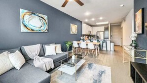 Ein modernes Wohnzimmer mit grauem Sofa, einem Glastisch und einem Deckenventilator.