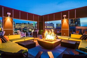 A rooftop lounge with a fire feature, seating, and city views.