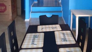 Een eethoek met een tafel gedekt voor vier personen, een witte deur op de achtergrond en blauwe wanden.