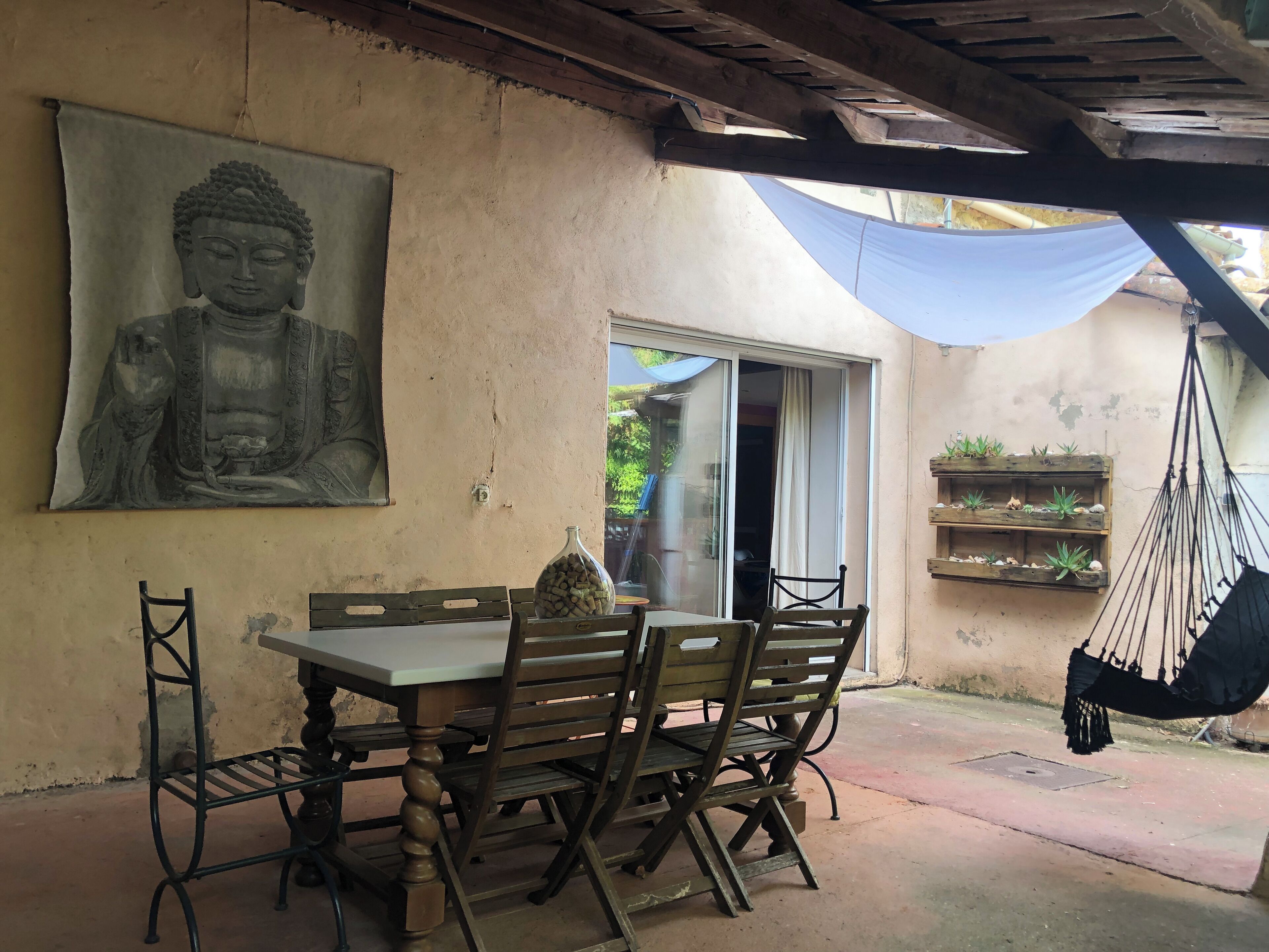 A dining area with a table and chairs, a Buddha statue, a hammock, and a window with a view.