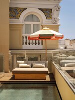 A balcony with a bed, a glass railing, and a pool.