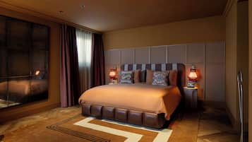 Habitación de hotel con una cama grande, dos lámparas de noche, un ventanal con cortinas y vistas a la ciudad.