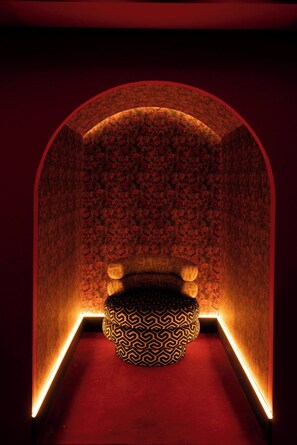 A room with a red carpet, a patterned wall, and a circular seating area with a geometric design. - Nômade Temple Madrid (Madrid)