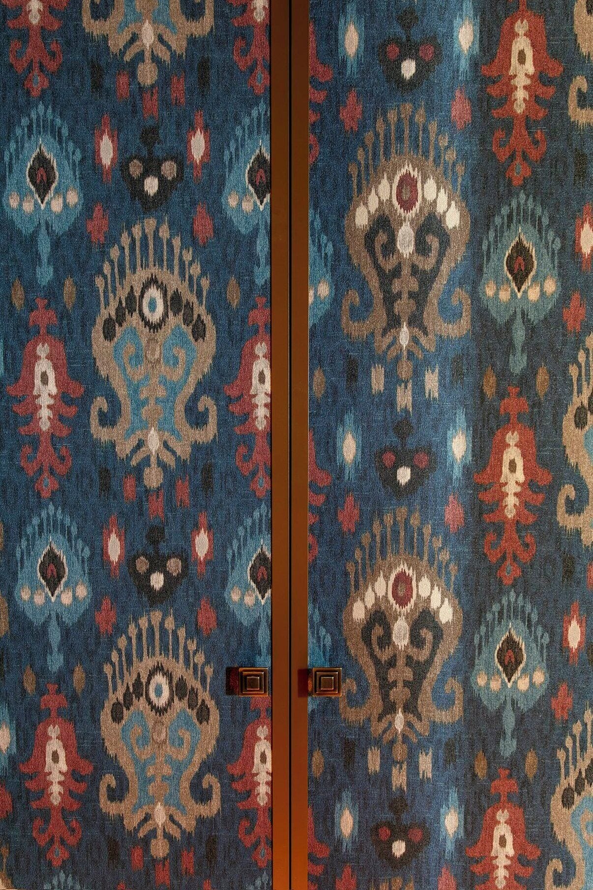 A room with a patterned carpet, a wooden door, and a brown wall.