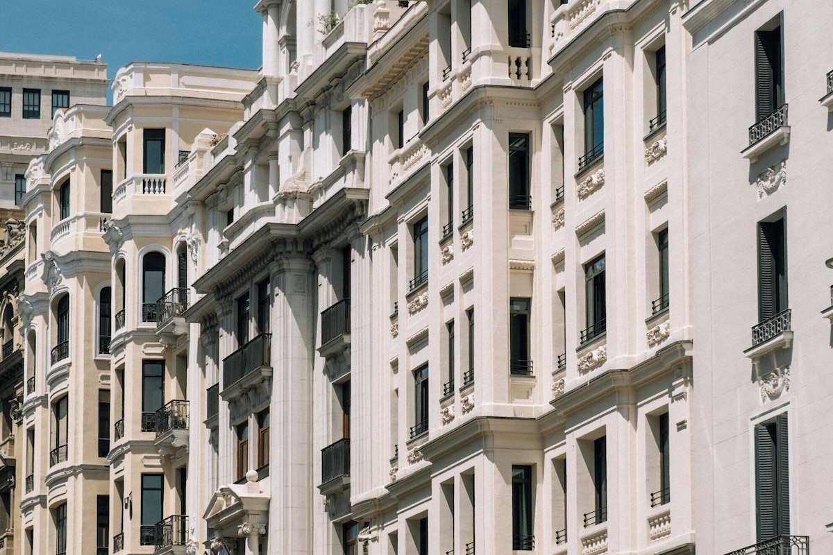 A row of white buildings with classical architecture, featuring multiple stories, balconies, and large windows.