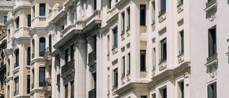 Une rangée de bâtiments blancs à l’architecture classique, dotés de plusieurs étages, de balcons et de grandes fenêtres.