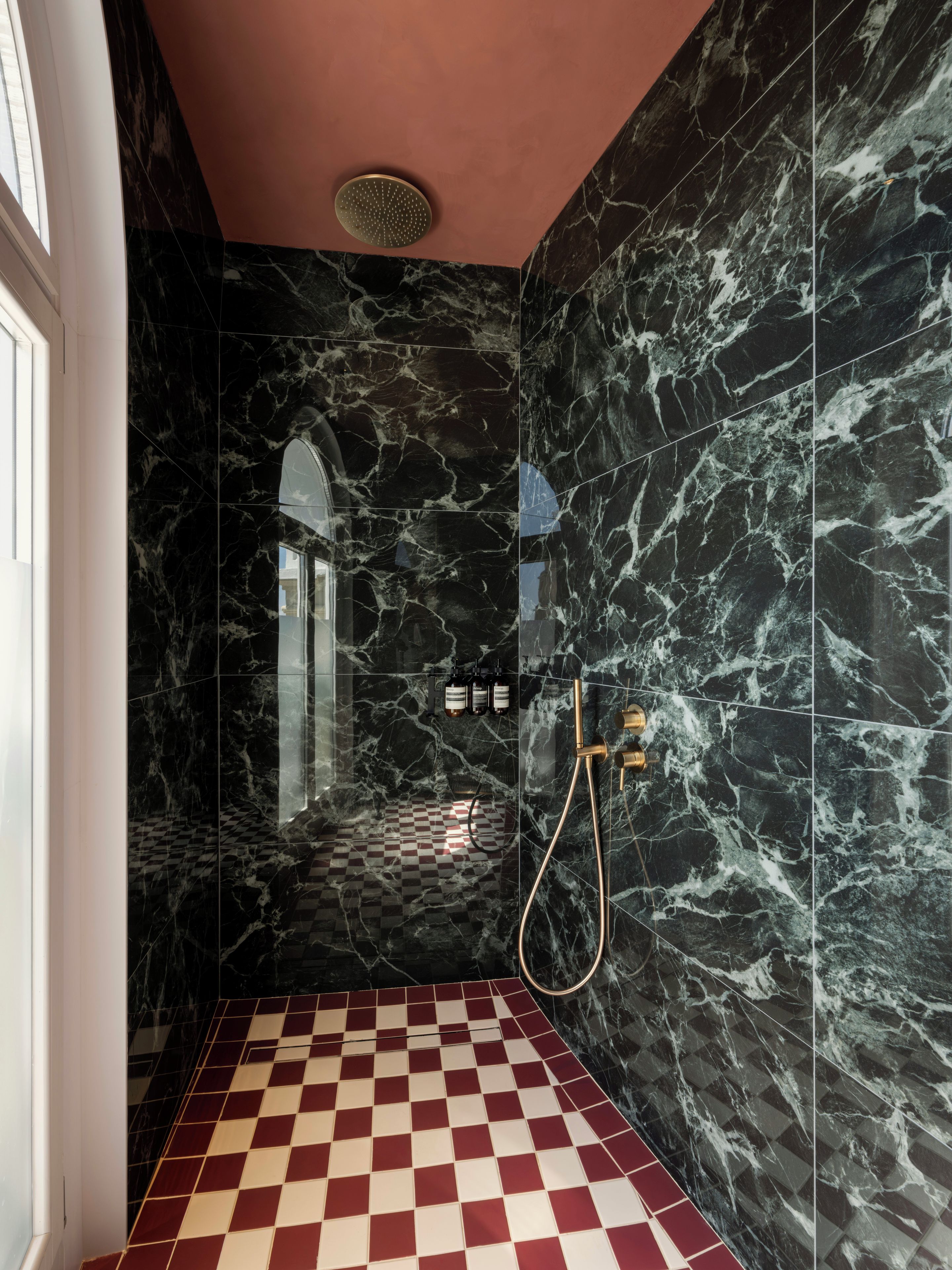 A bathroom with black marble walls, a checkered floor, and a shower area with a handheld showerhead.