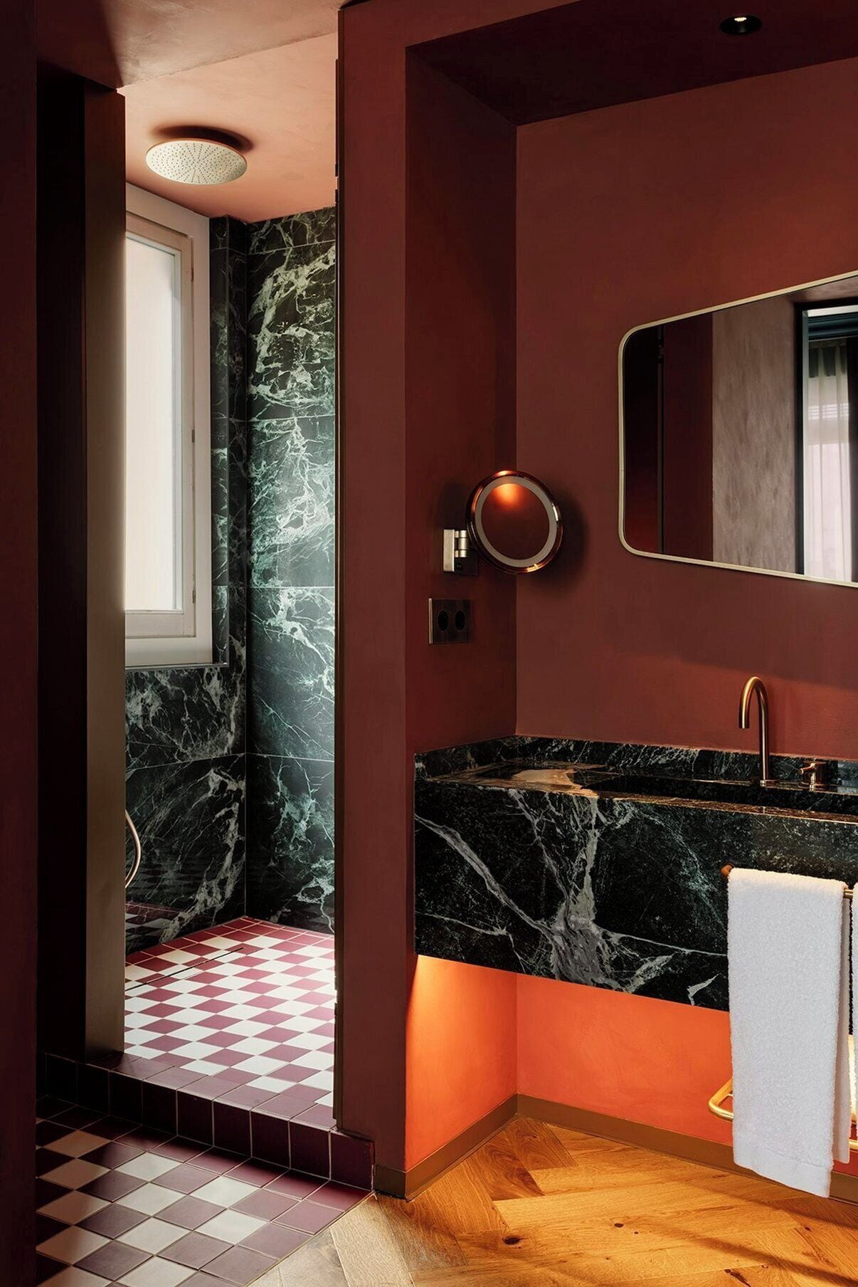 A modern bathroom with a marble wall, a round mirror, and a wooden floor.