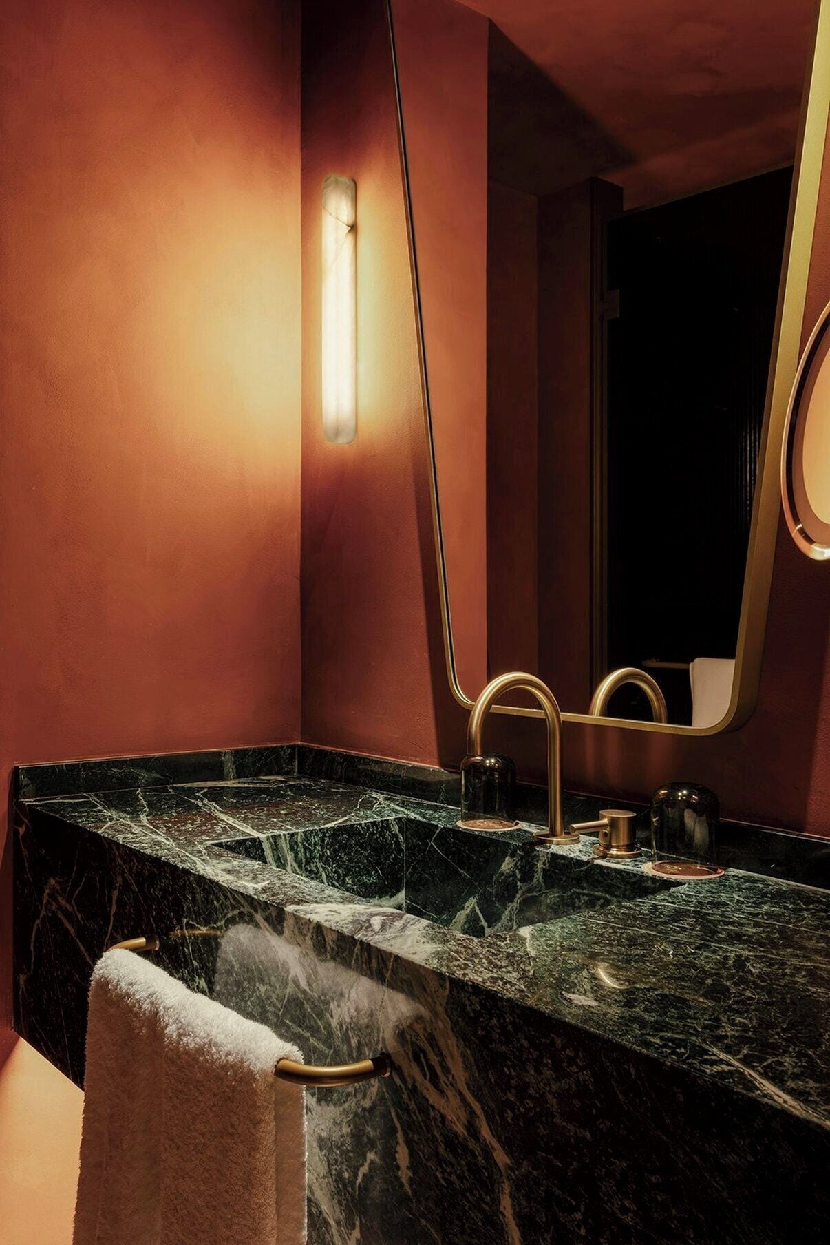 A bathroom with a marble countertop, a towel rack, a mirror, and a wall-mounted light fixture.